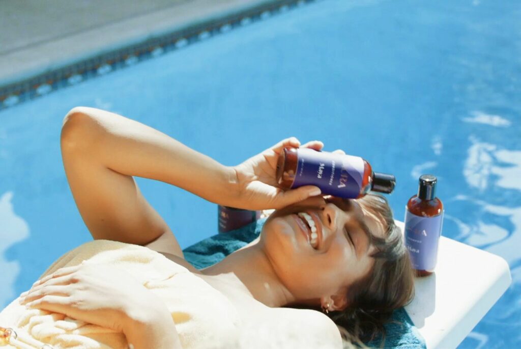 Girl laying on diving board, laughing, with AURA bottles in her hand. 