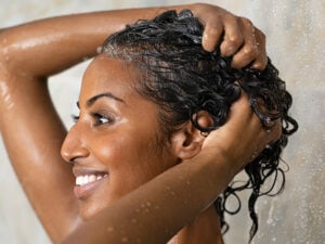 Woman of color with hands in her hair washing her curly hair with high-quality ingredients.