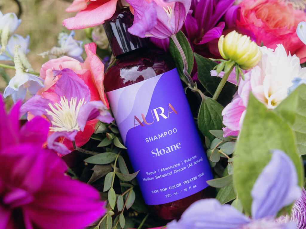 AURA personalized shampoo bottle laying in brightly colored flowers.