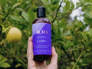 Hand holding a bottle of AURA's personalized shampoo in front of a leafy pear tree.