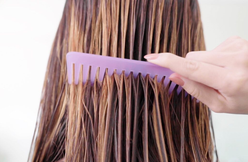 Wet brunette hair being combed through with purple wide tooth comb.