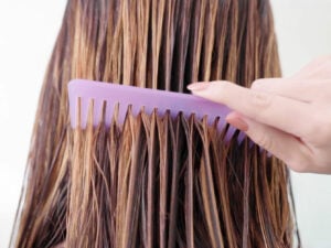 Wet hair being brushed through with purple wide tooth comb