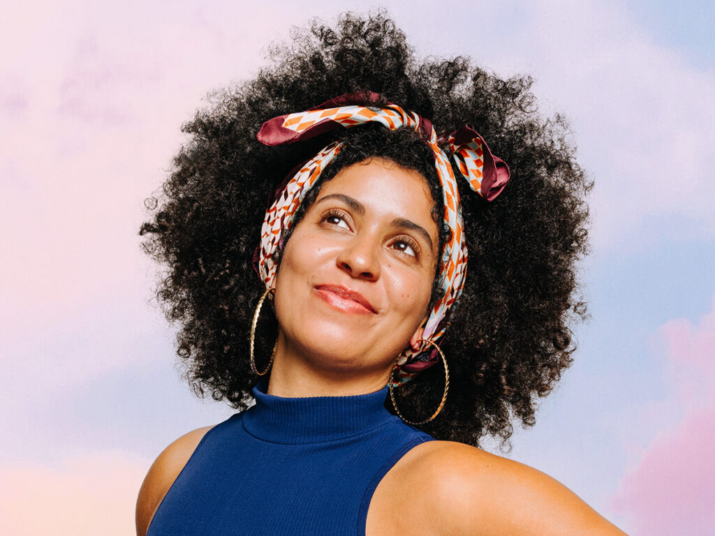 Woman with curly hair wearing a silk scarf as a headband.